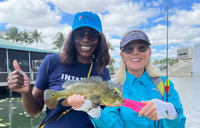 Joyce David and Robin Krueger holding a peacock bass along the water for Ladies Let's Go Fishing